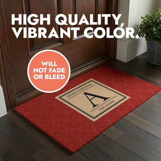 A red doormat with geometric pattern printed on the background with a square in the middle featuring 'Merry Christmas' Text and custom letter and family name.
