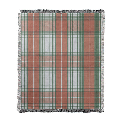 Traditional tartan style plaid in green and red with white printed on a woven cotton-polyester blanket with decorative fringed edges.